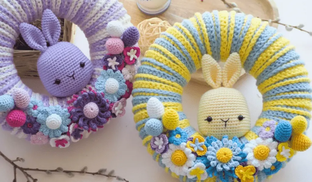 Two crochet Easter wreaths, one that is purple and white and one is yellow and blue, both having amigurumi bunny heads in the middle.