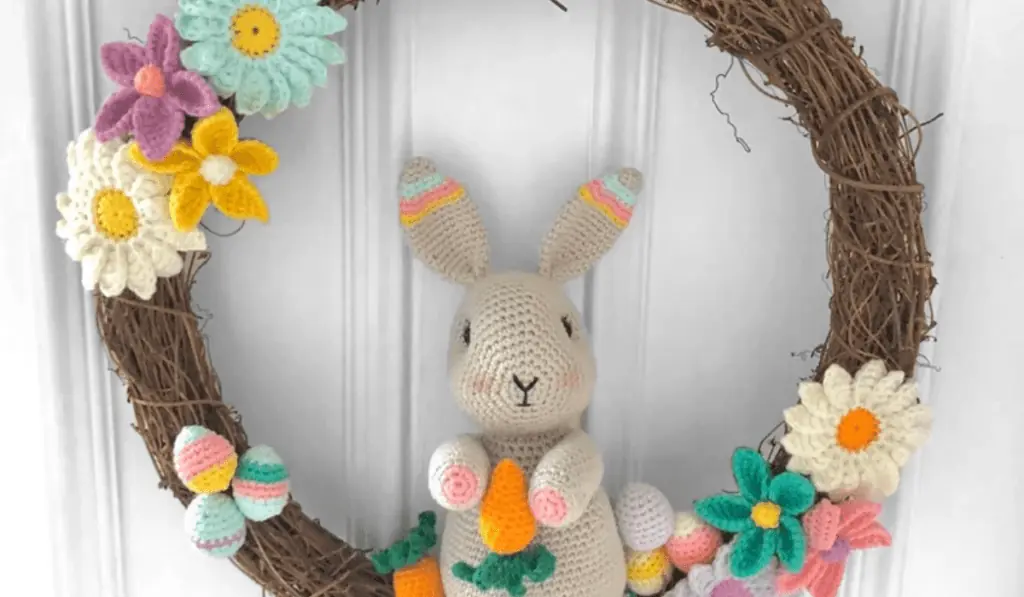 A crochet wreath with an amigurumi bunny in the middle surrounded by small eggs and crochet flowers.