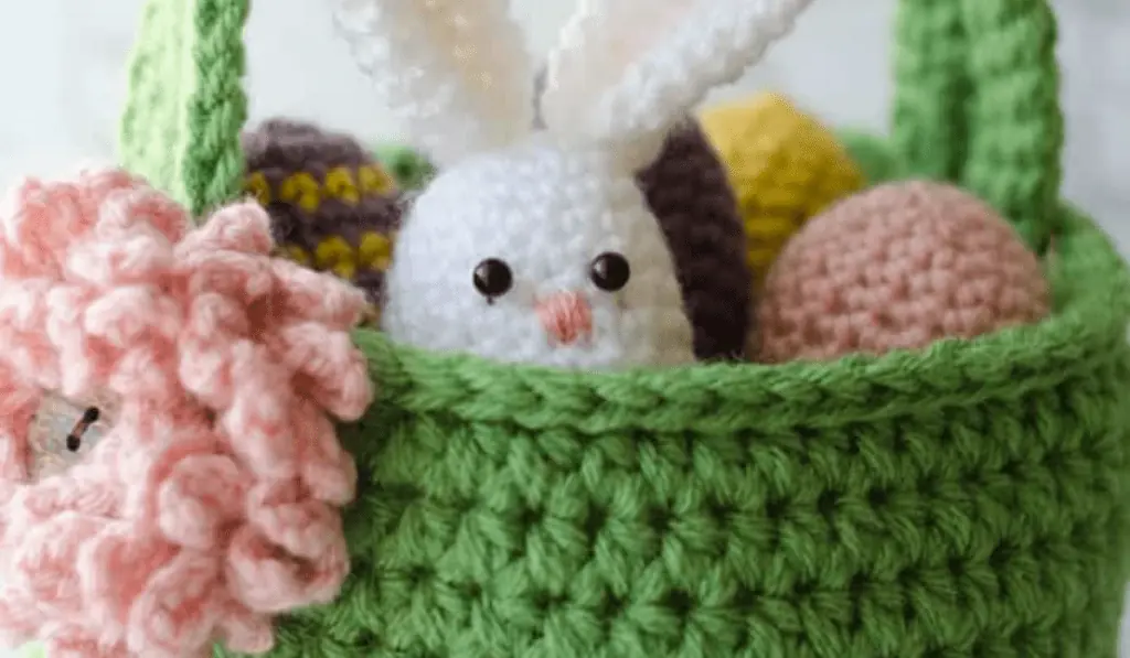 A green crochet Easter basket with a bunny that's shaped like an egg and many crochet eggs in the basket