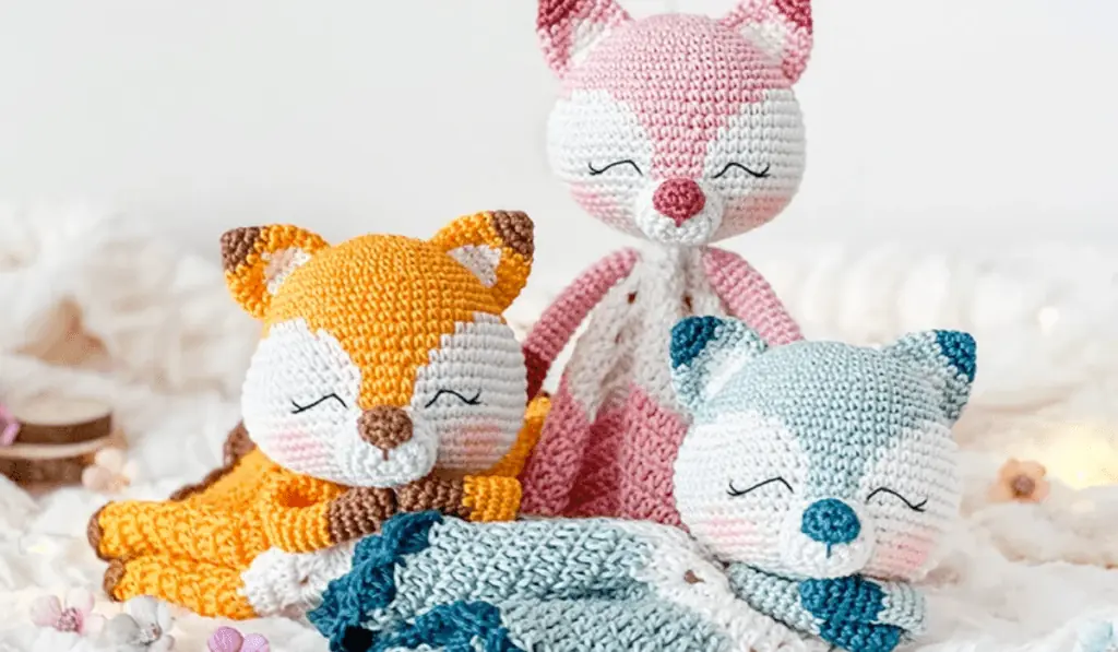 Three crochet fox loveys in pink, blue, and orange.