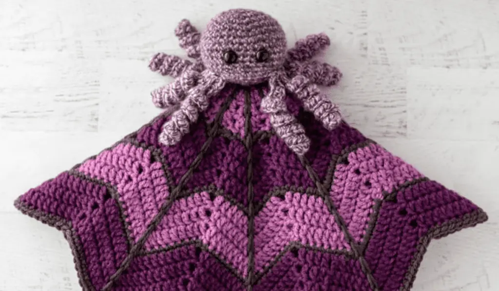 A crochet spider lovey with different shades of purple in the blanket.