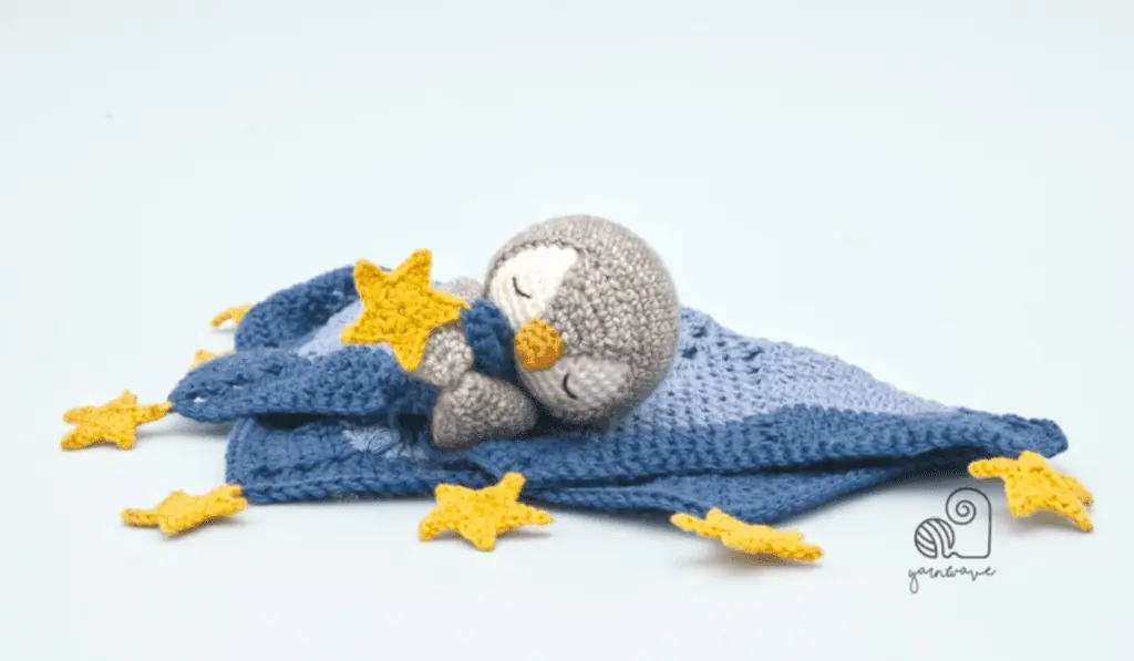 a crochet penguin lovey where the penguin is holding onto a bit of the blanket.