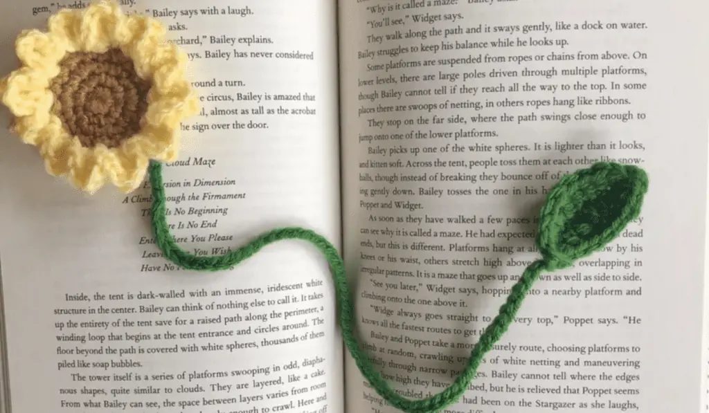 A crochet sunflower bookmark laying on a book.
