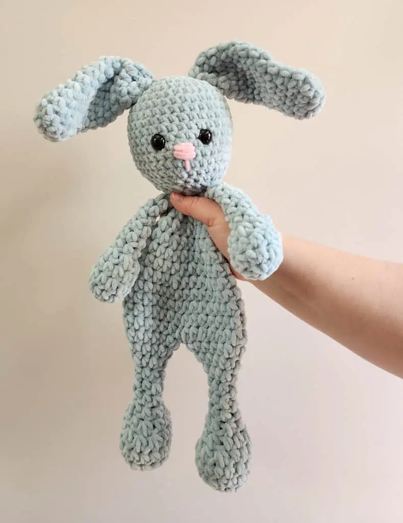 blue bunny crochet snuggler with pink nose held without outreached hand