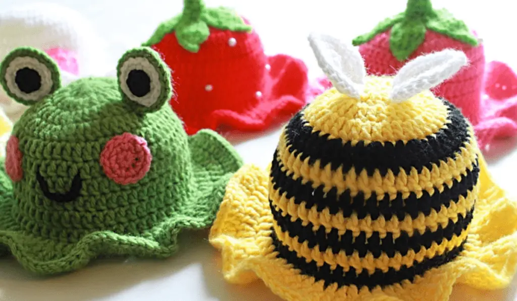 Four crochet bucket hats, one that looks like a frog, one that looks like a bee, and two that look like strawberries.