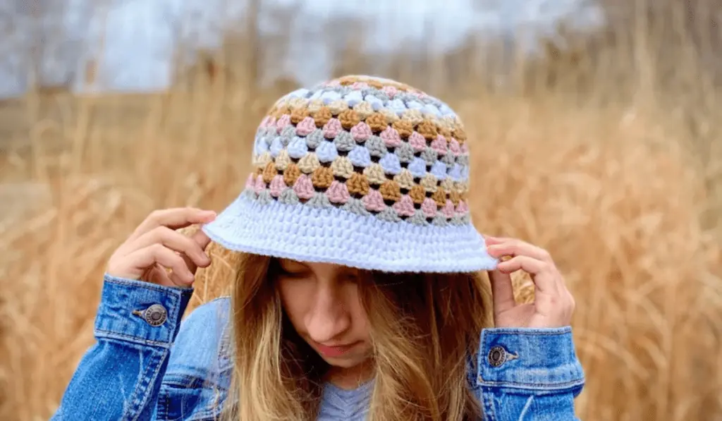 A crochet bucket hat with rows of stitches in pink, yellow, orange, white, and grey with a white brim.