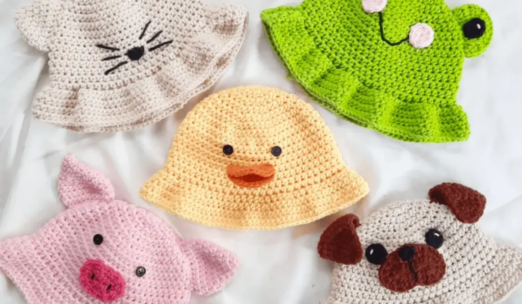 Five crochet bucket hats, one that looks like a cat, one that looks like a frog, one that looks like a duck, one that looks a pig, and one that looks like a dog.