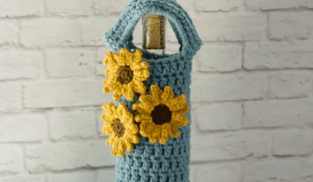 A crochet wine cozy with a blue body and three small sunflowers