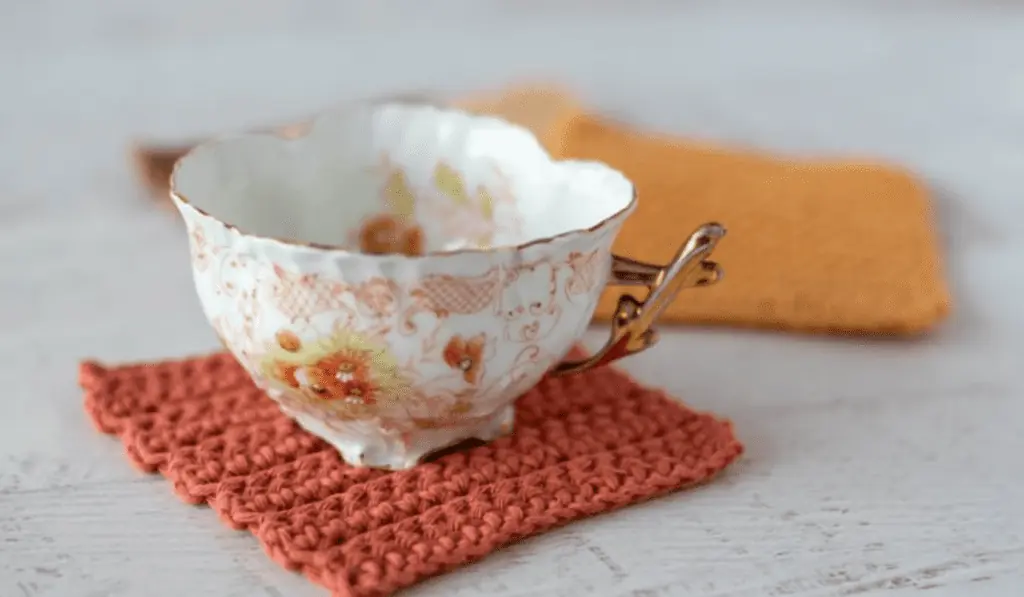 A pink square crochet coaster with a tea cup on top.