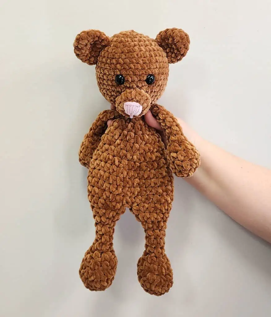 Brown Bear Snuggler in velvet yarn held up against wall with hand