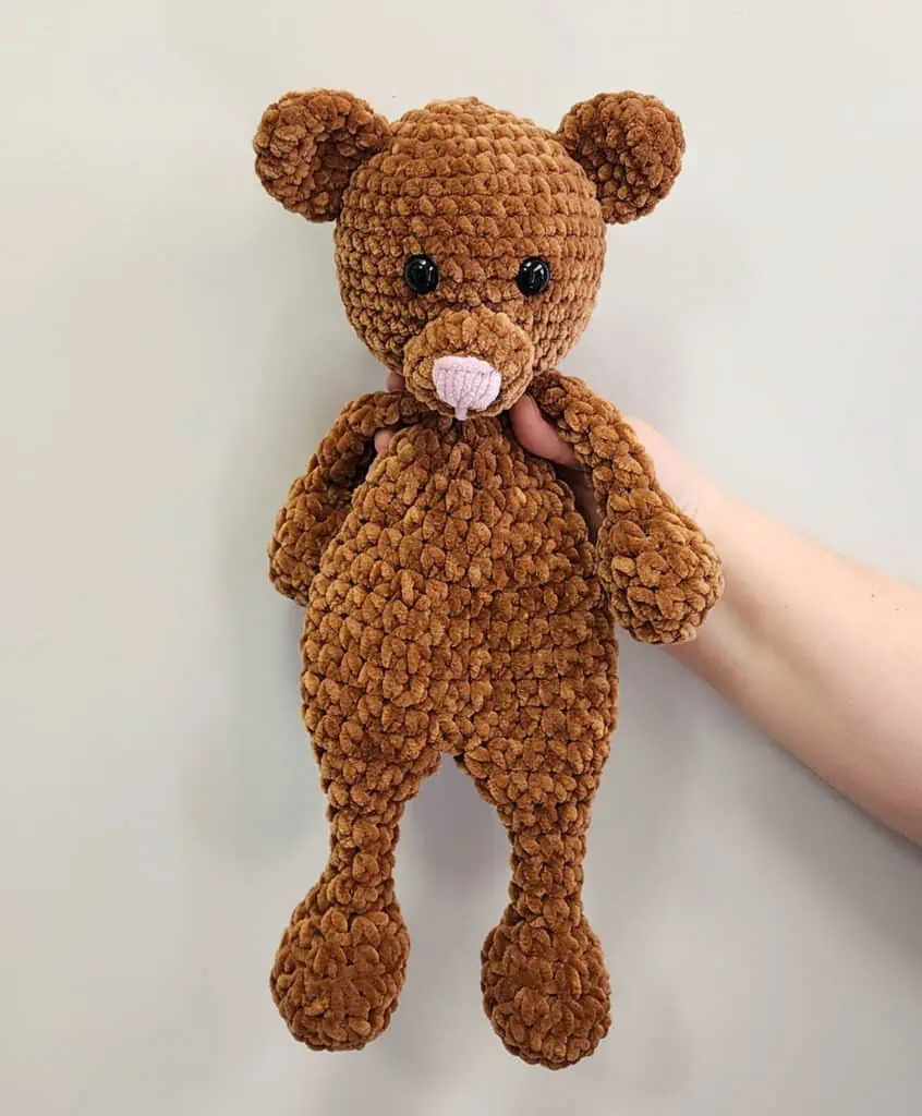Brown Bear Snuggler in velvet yarn held up against wall with hand