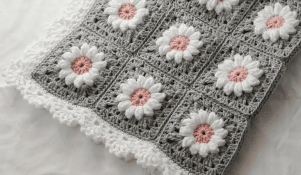 A grey crochet baby blanket pattern with flower granny squares with pink middles and white petals and a white border.
