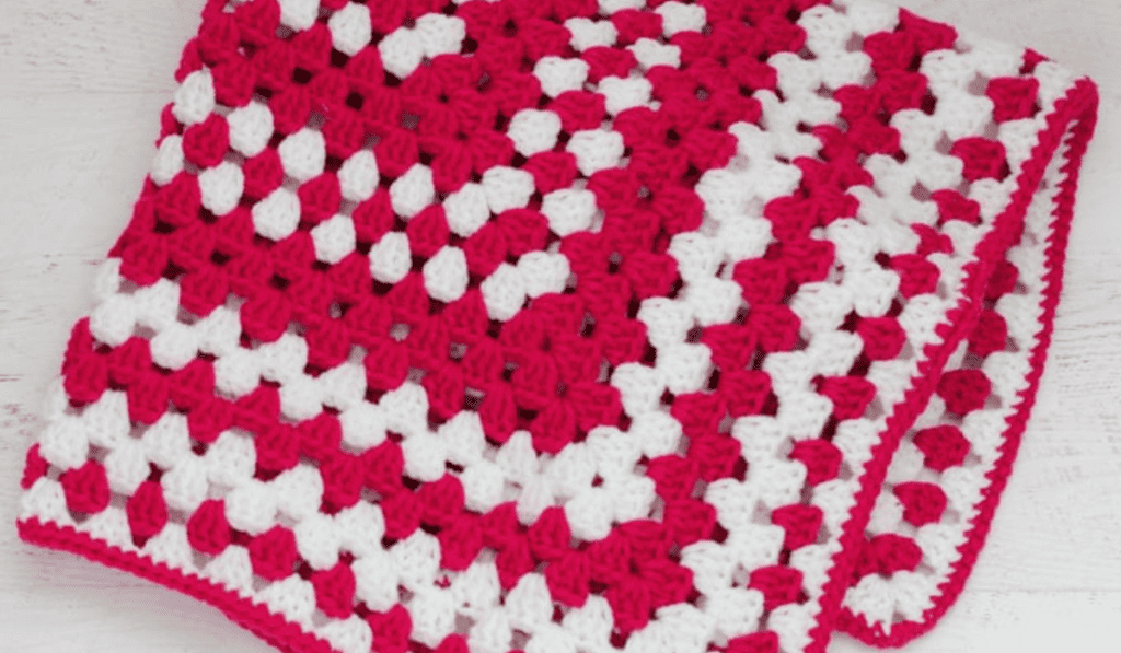 A pink and white crochet baby blanket pattern made as a large granny square.