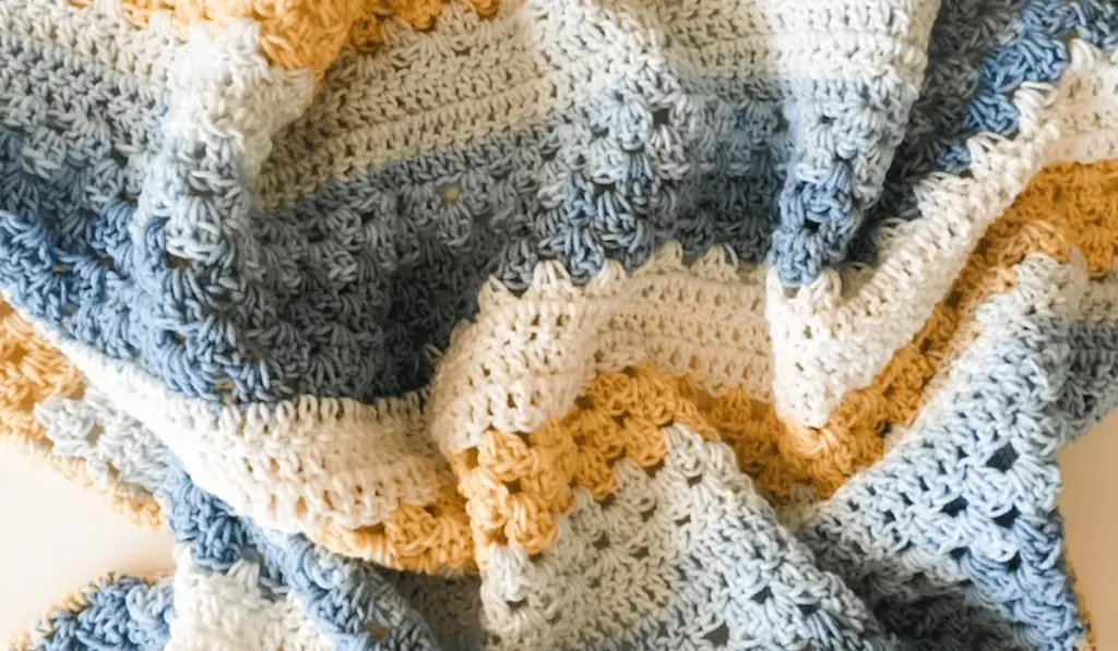 A crochet baby blanket with stripes of white, light blue, dark blue, and yellow.
