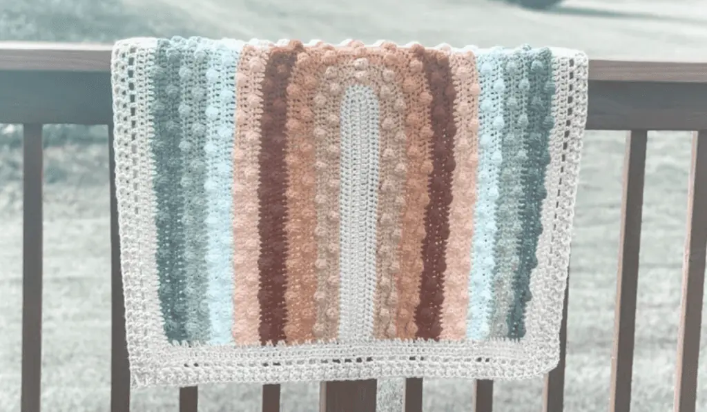 A crochet baby blanket that features a rainbow with puff stitches on it.