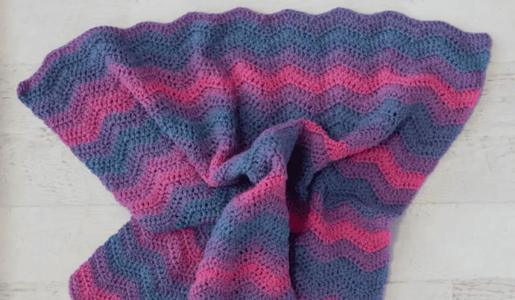 A ripple crochet baby blanket pattern that features pink, blue, and purple yarn.