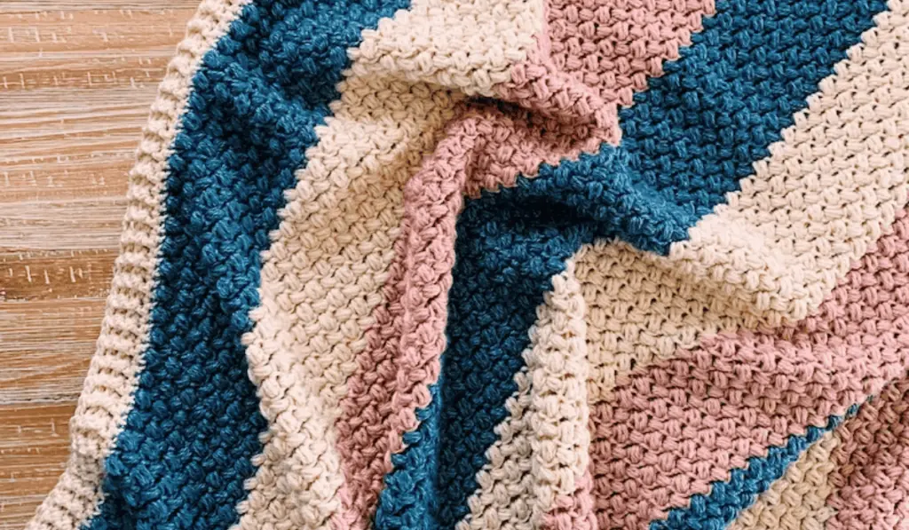 A bold color-blocked baby blanket that features blue, white, and pink yarn stripes.