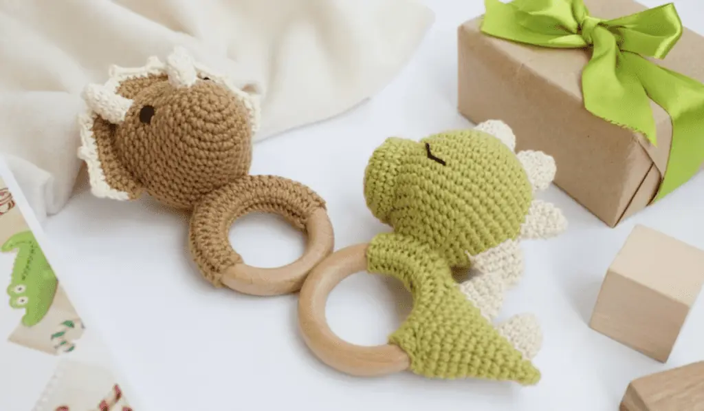 Two crochet dinosaur rattles, one brown and one green.