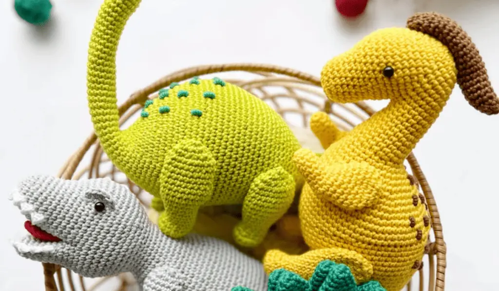 Three crochet dinosaurs, one grey, one green, and one yellow.