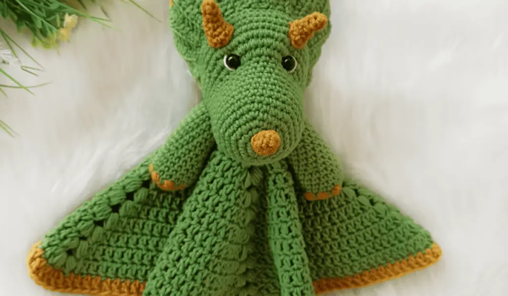 A green crochet dinosaur blanket with a green body and gold accents.