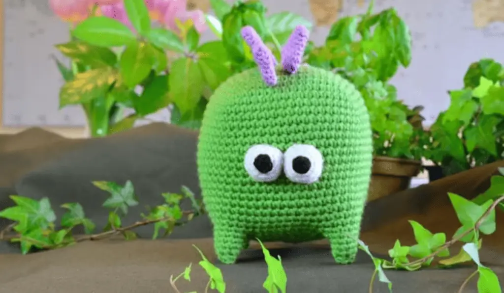 A square shaped crochet dinosaur with big googly eyes