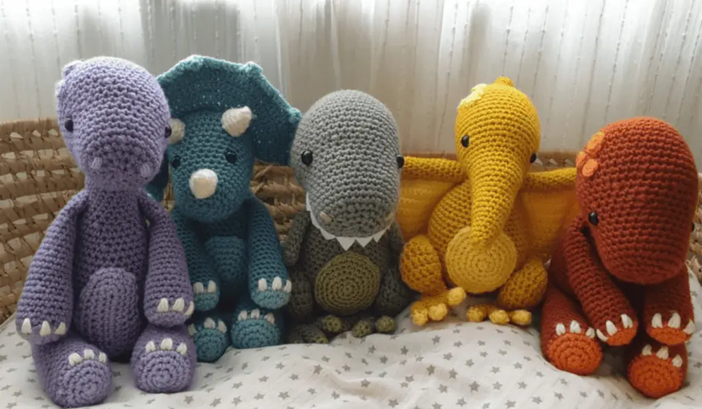 Five different types of crochet dinosaurs in purple, blue, grey, yellow, and red.