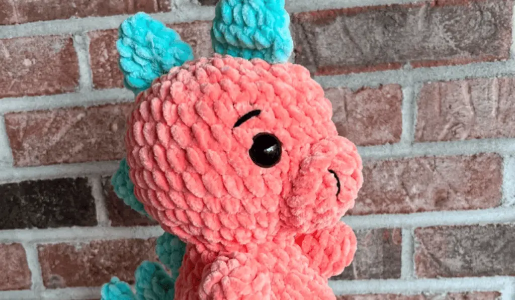 A pink chunky yarn dinosaur with blue spikes