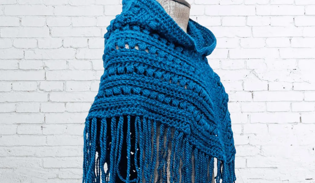 A blue crochet poncho with different bobble details.