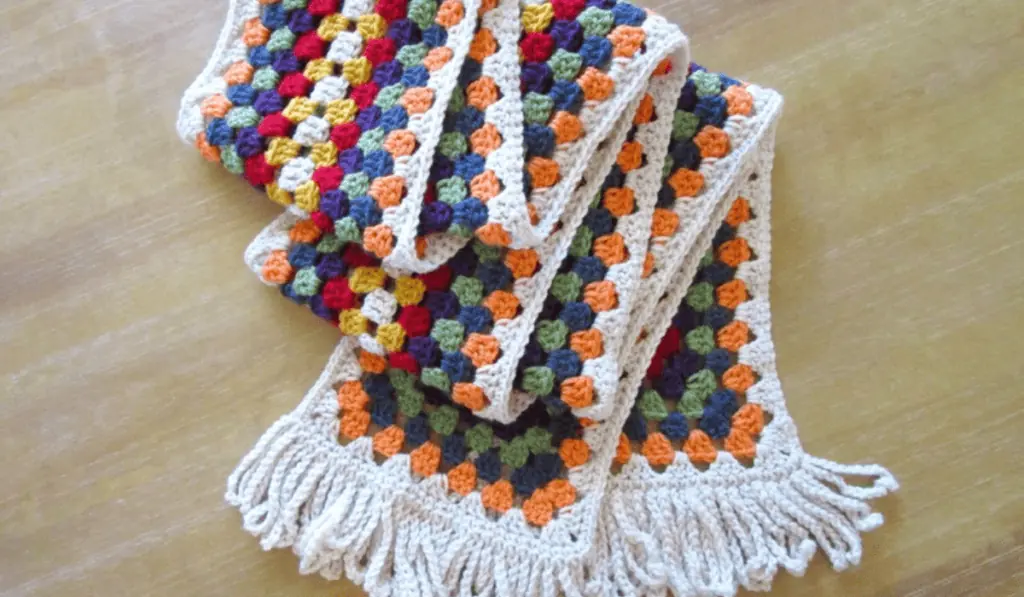 A granny stitch scarf with white, orange, blue, green, and yellow yarn.