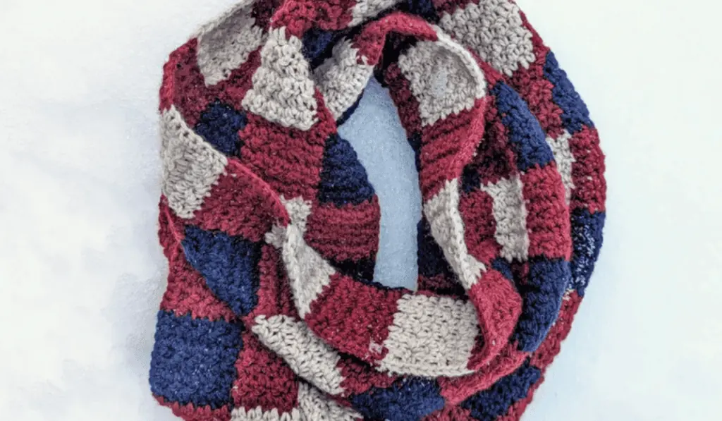 A crochet scarf with a checkered design which includes white, blue, and red yarn.