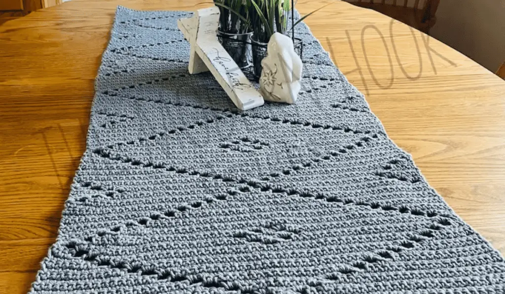 A crochet table runner in grey yarn with large dimonds in the pattern.