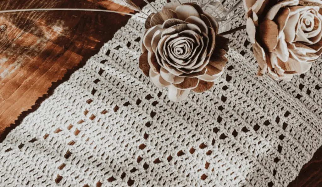 A crochet table runner with small diamond cut outs with white yarn.