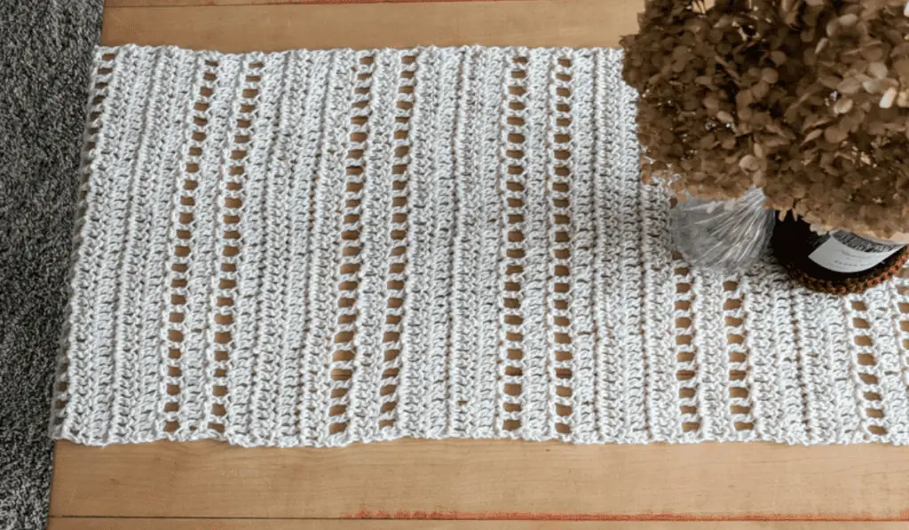 A white crochet table runner with rows of cut outs.