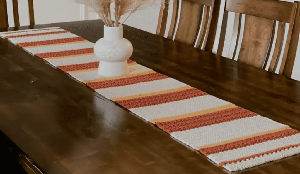 A fall looking crochet table runner with white, orange, and yelllow yarn in blocks of color.