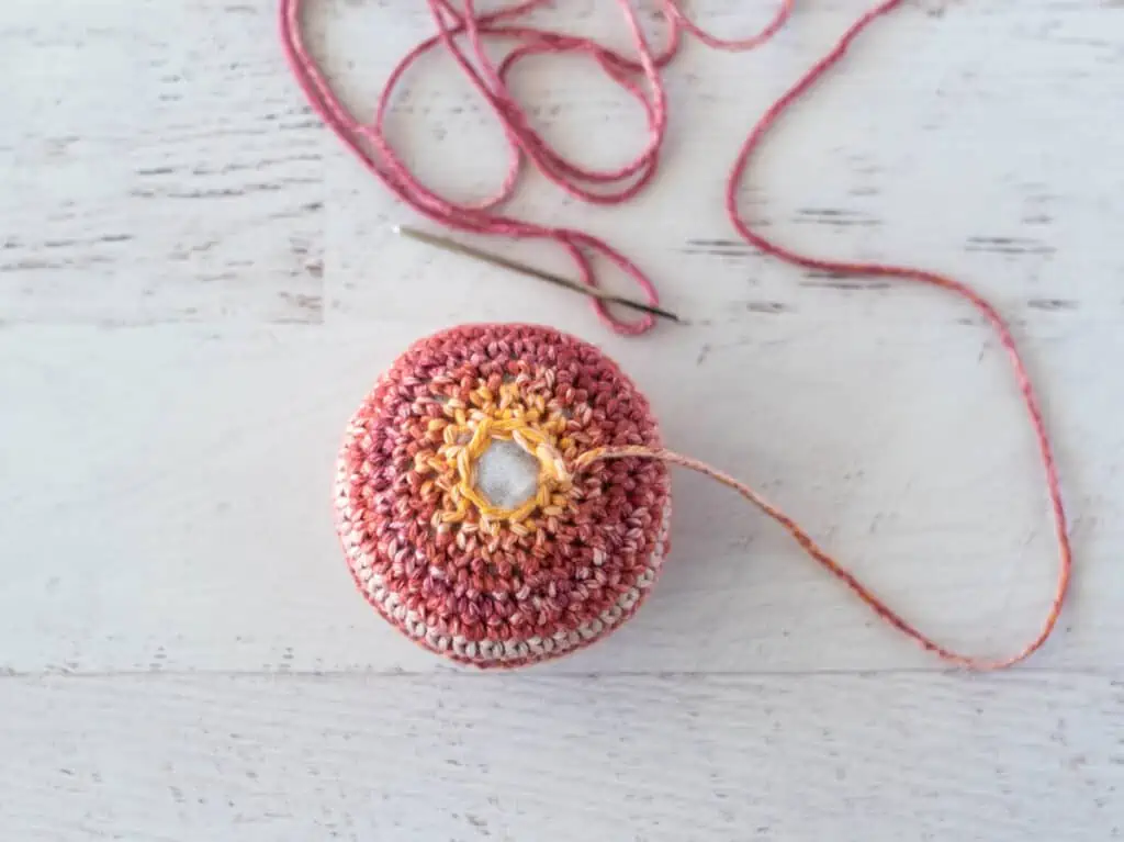 crochet sphere out of orange tone yarn. Yarn end threaded on yarn needle.