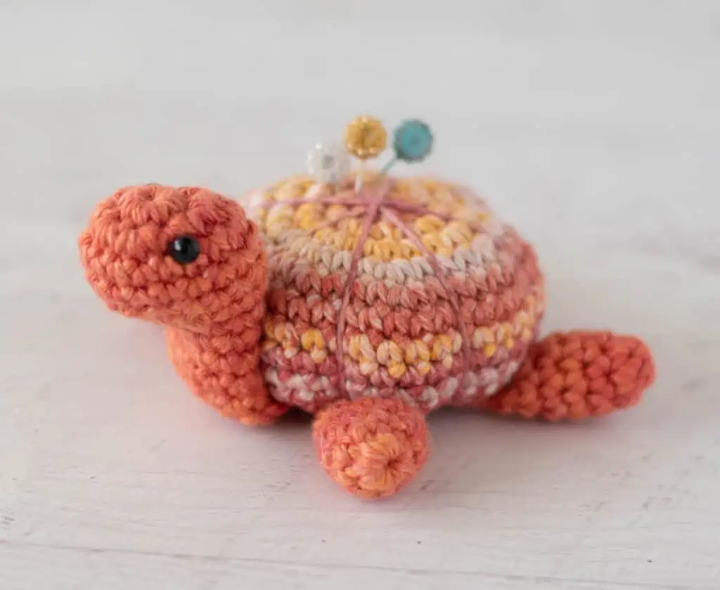 Orange tone crochet turtle pincushion with floral decorative pins on top