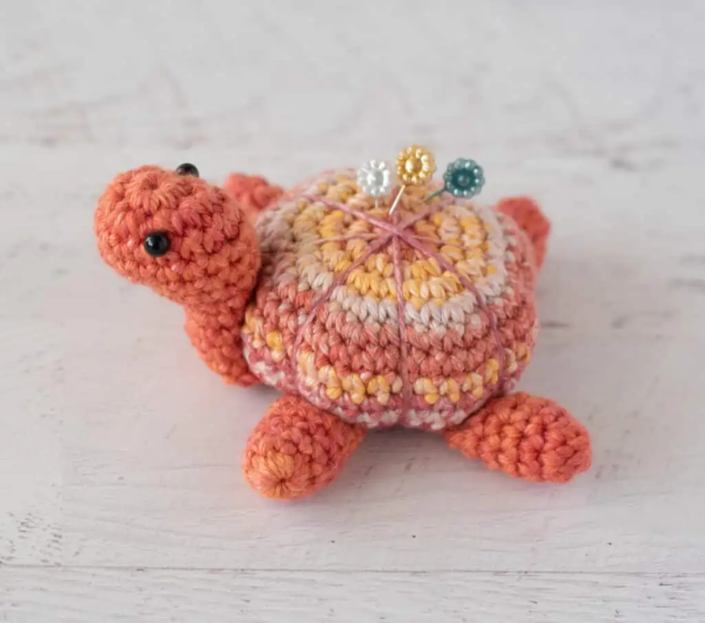 Orange tone crochet turtle pincushion with floral decorative pins on top