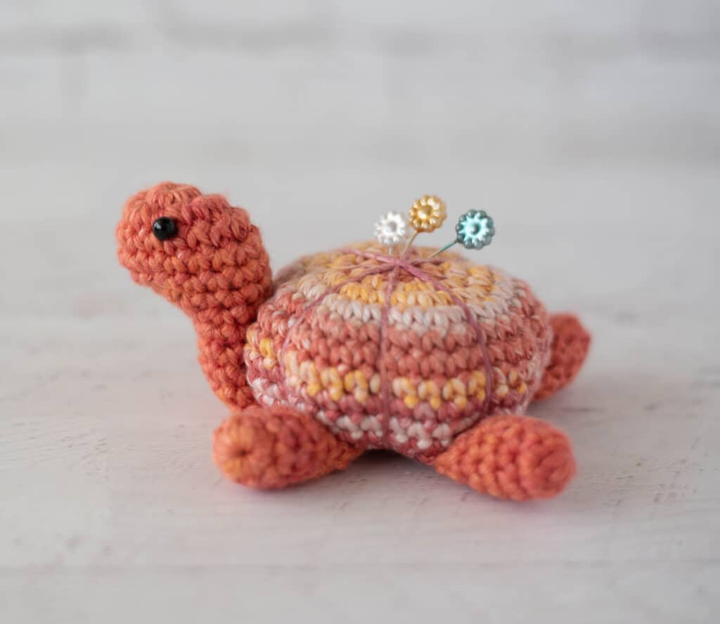 Orange tone crochet turtle pincushion with floral decorative pins on top