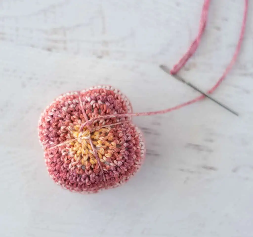 Cinching crochet sphere to make a pumpkin shape. orange and yellow yarn with yarn needle.