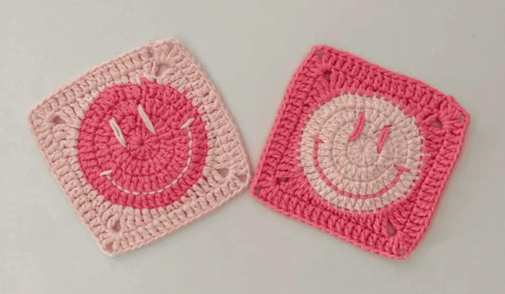 Two smiley face granny squares, one with a light pink border and a dark pink middle, then the other granyy square is the opposite.