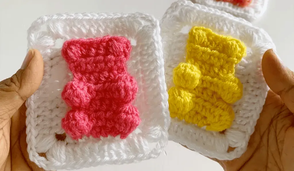 Two gummy bear granny squares, one with a pinky gummy bear and one with a yellow gummy bear.