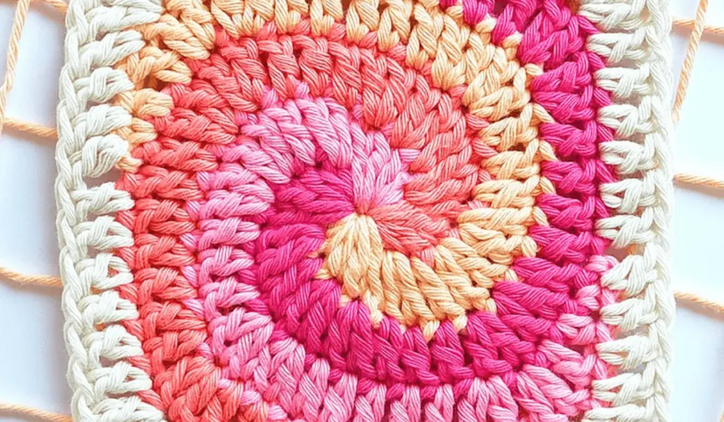 A swirling granny square with different lines of color, include a peach, a hot pink, a light pink, and a coral.