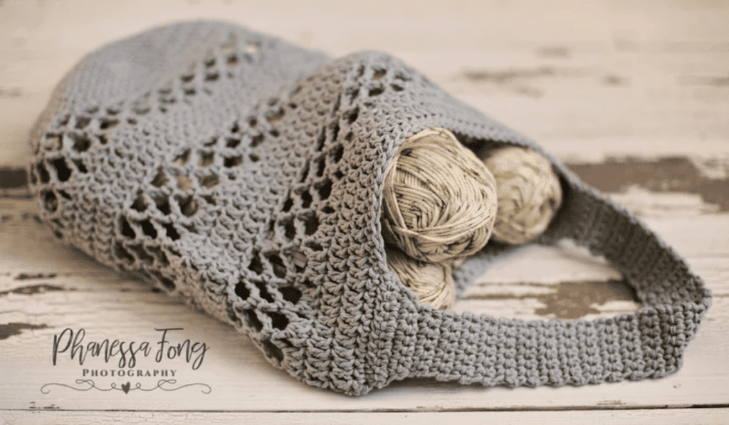 A grey crochet market bag with rows of chain spaces as details.