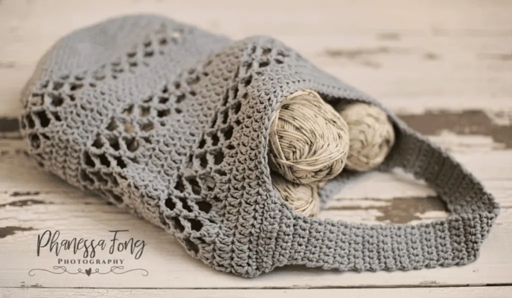 A grey crochet market bag with rows of chain spaces as details.