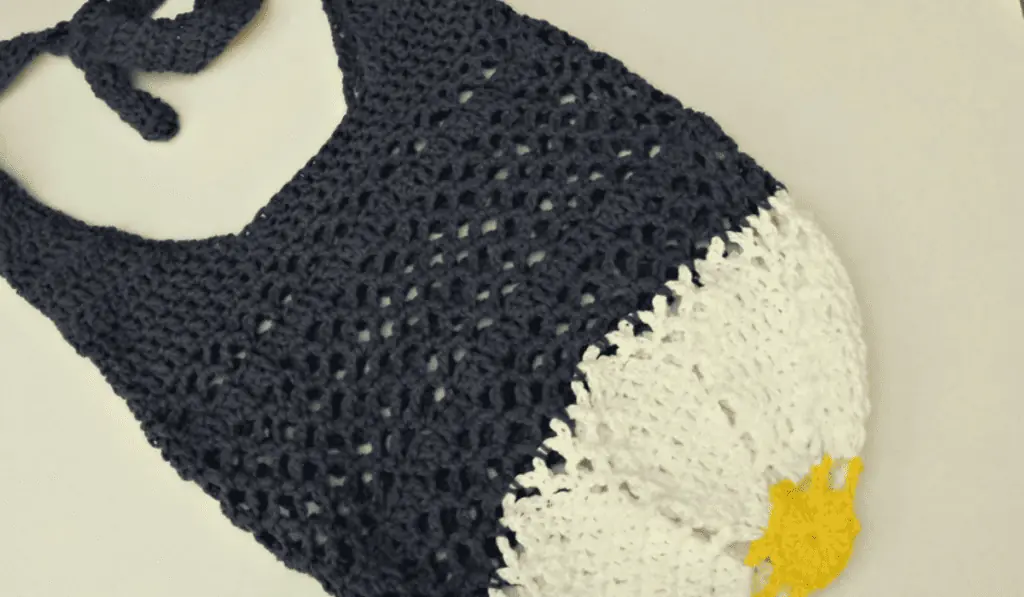 A crochet market bag with a dark blue body, a white bottom, and a yellow center.
