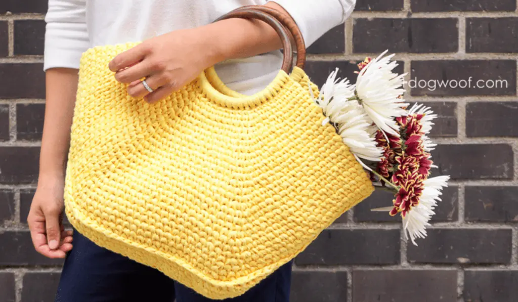 A yellow oversized crochet bag with a wooden wrist hole.