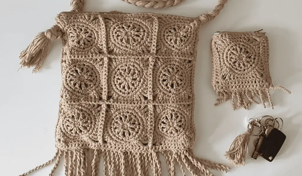 A beige crochet bag pattern with tasels along the bottom and nine squares with circle designs in the squares. There is also a beige coin pouch as well.