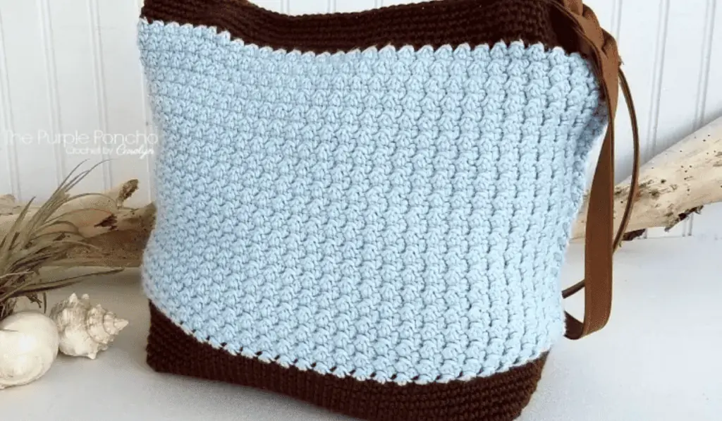 A blue oversized crochet bag with rows of brown on the bottom and on the top.