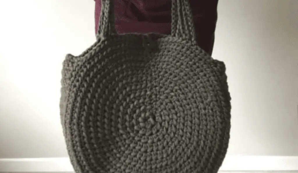 A circle crochet bag made out of dark grey yarn.