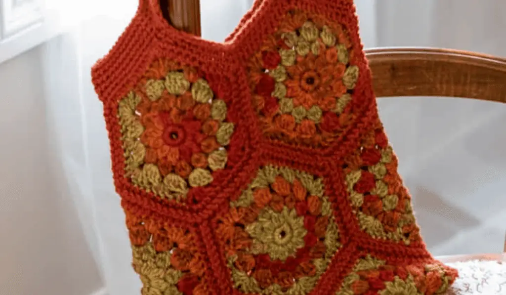 A crochet tote bag pattern with granny squares made out of red, orange, and green yarn.